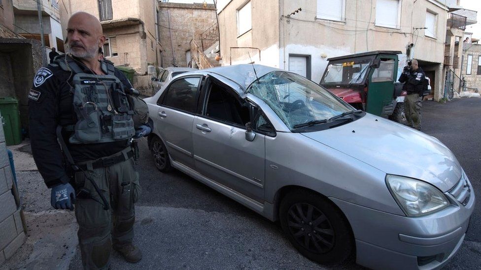 Сотрудник израильских сил безопасности стоит рядом с автомобилем в северной израильской деревне Фассута, который был поврежден ракетой, выпущенной из Ливана (6 апреля 2023 г.)