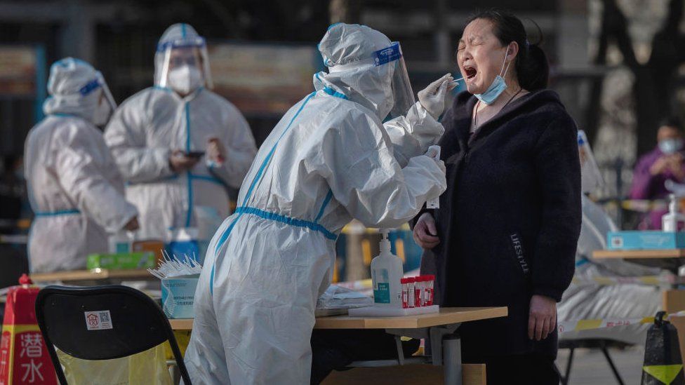 A health worker wears protective gear as she gives a nucleic acid test to detect COVID-19 on a local resident at a mass testing site after new cases were found, on April 6, 2022