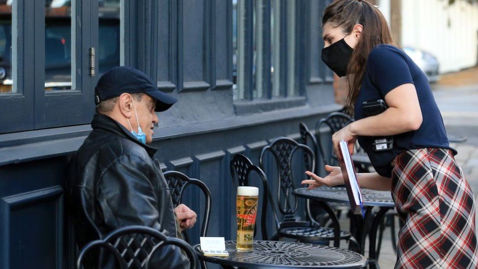 A waitress serves a man a beer outside a pub