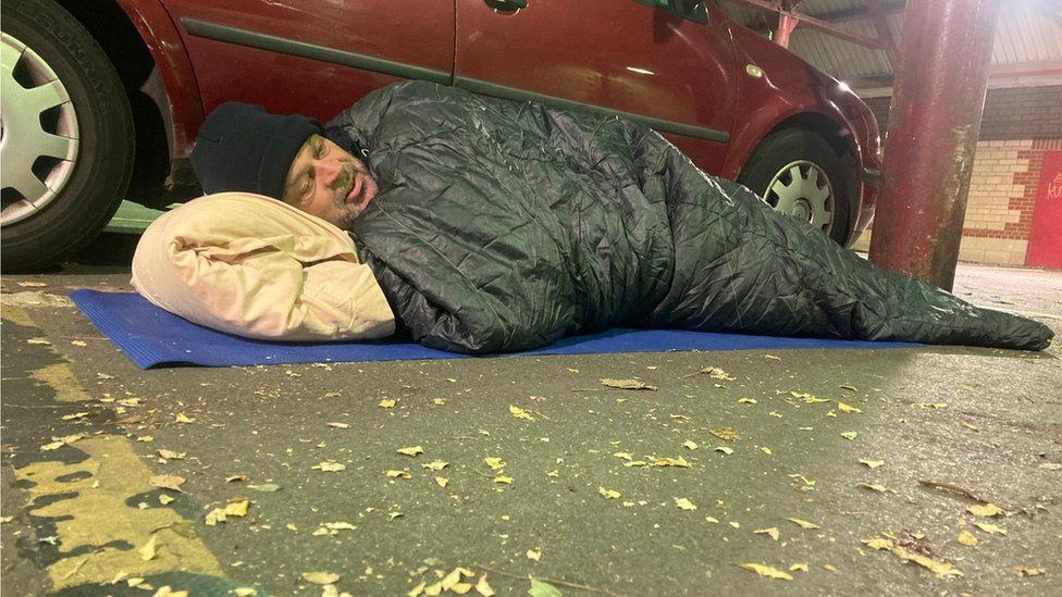 Brian Tubb sleeping near a car