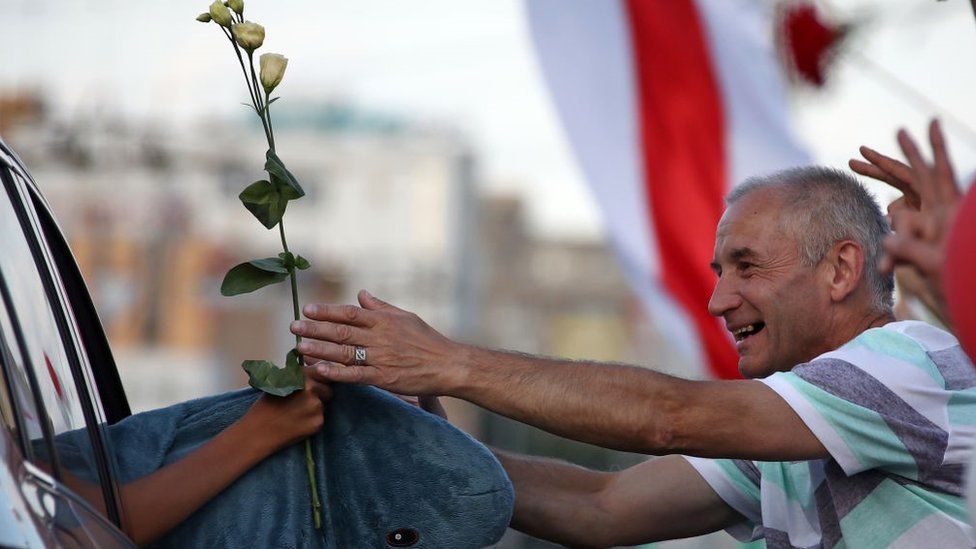 A man presents flowers to passing cars' passengers during an opposition event