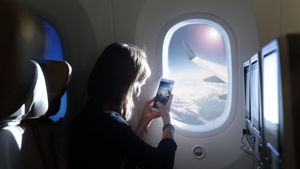 A woman on her phone looking out of a plane window