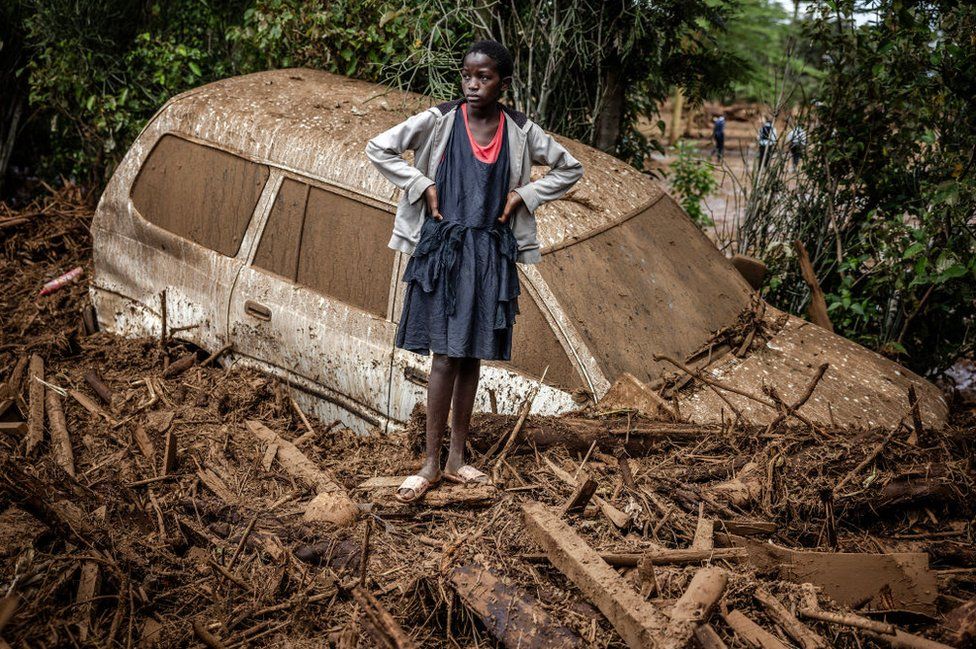 A girl looks on next to a damaged car buried in mud in an area heavily affected by torrential rains and flash floods in the village of Kamuchiri, near Mai Mahiu, on April 29, 2024.