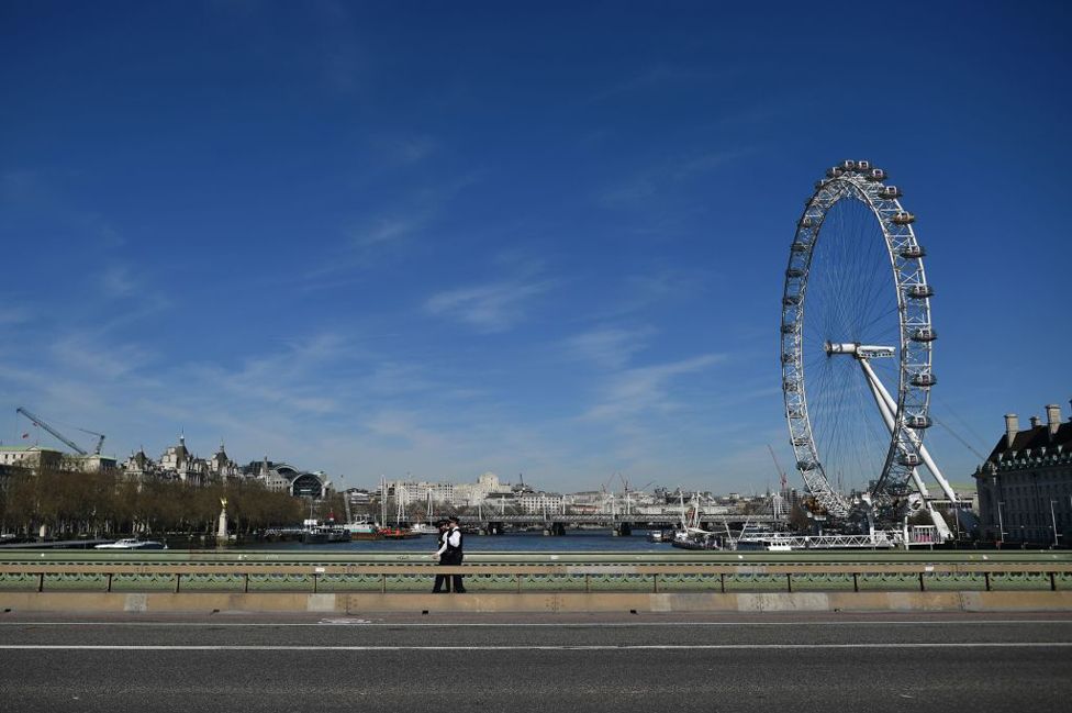 Two police officers walk over a deserted Westminster Bridge with the London Eye seen behind, in central London, 23 March 2020