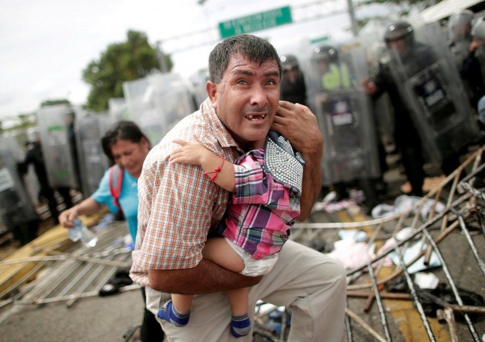 A Honduran man protects his baby amid clashes between migrants and Mexican Police