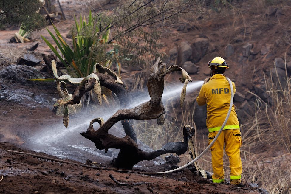 A Maui County firefighter fights flare-up fires in a canyon in Kula on Maui