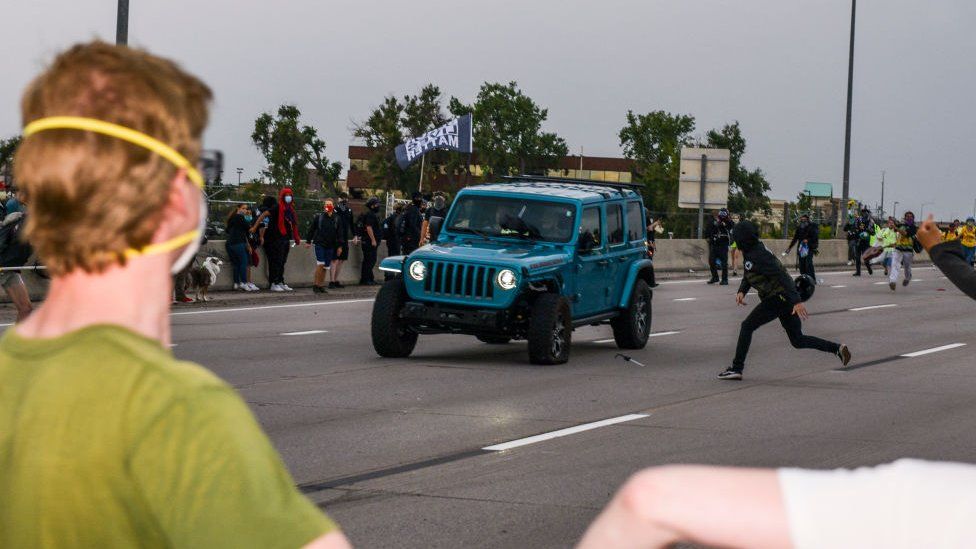 People run to get out of the way as a Jeep speeds through a crowd of people protesting in Aurora, Colorado