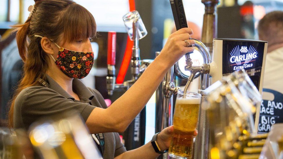 Woman wearing facemask pours a pint