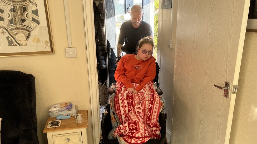 A man pushing a girl sitting in a wheelchair through a doorway
