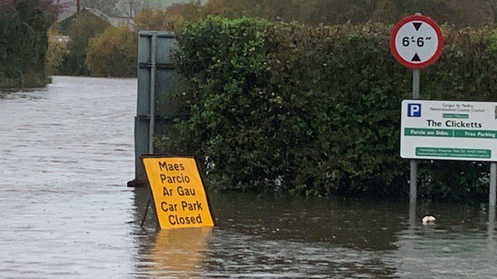 Closed sign floating in flood water in car park