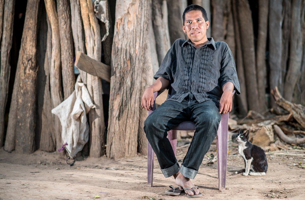 Chagabi Etacore sitting in a chair in the forest with a cat beside him