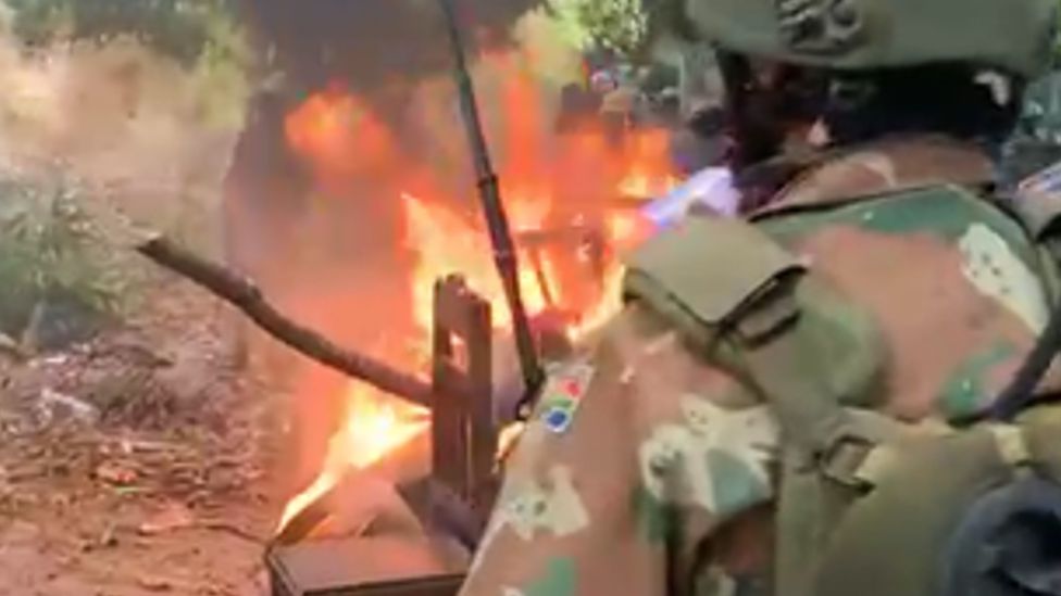 A screengrab from a video showing a man in army uniform with a South African flag in front of bonfire, which the SANDF says is believed to have been filmed in Mozambique