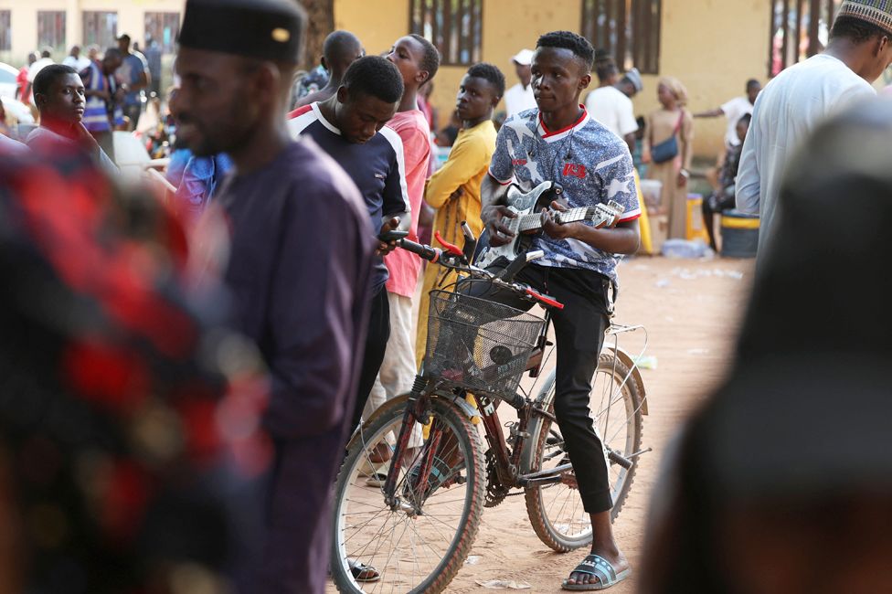 A man playing a guitar on a bicycle as he waits to vote in Yola, Nigeria - Saturday 25 February 20233