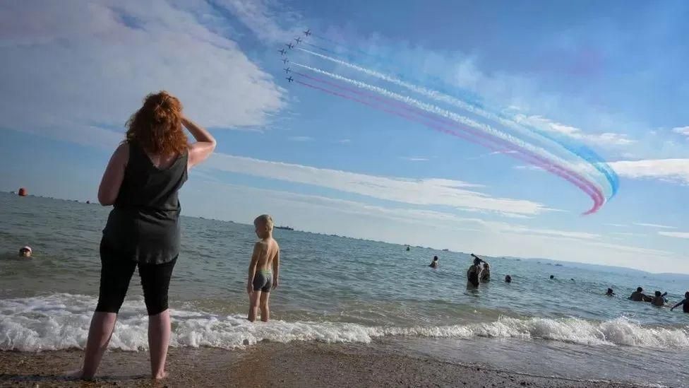 People standing in the sea at Bournemouth beach watching the Red Arrows overhead