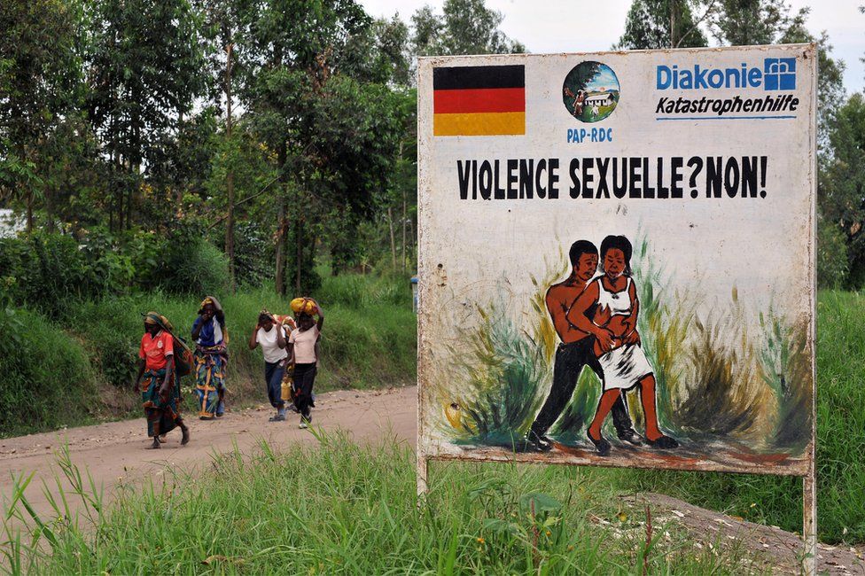 Congolese women walk past a sign opposing sexual violence on December 4, 2008 in Nyamilima, in Nord-Kivu, in the east of the Democratic Republic of Congo (DRC).