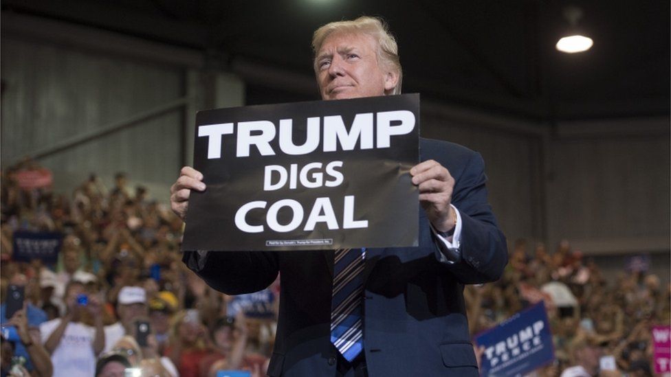 US President Donald Trump holds up a "Trump Digs Coal" sign as he arrives to speak during a Make America Great Again Rally at Big Sandy Superstore Arena in Huntington, West Virginia, August 3, 2017