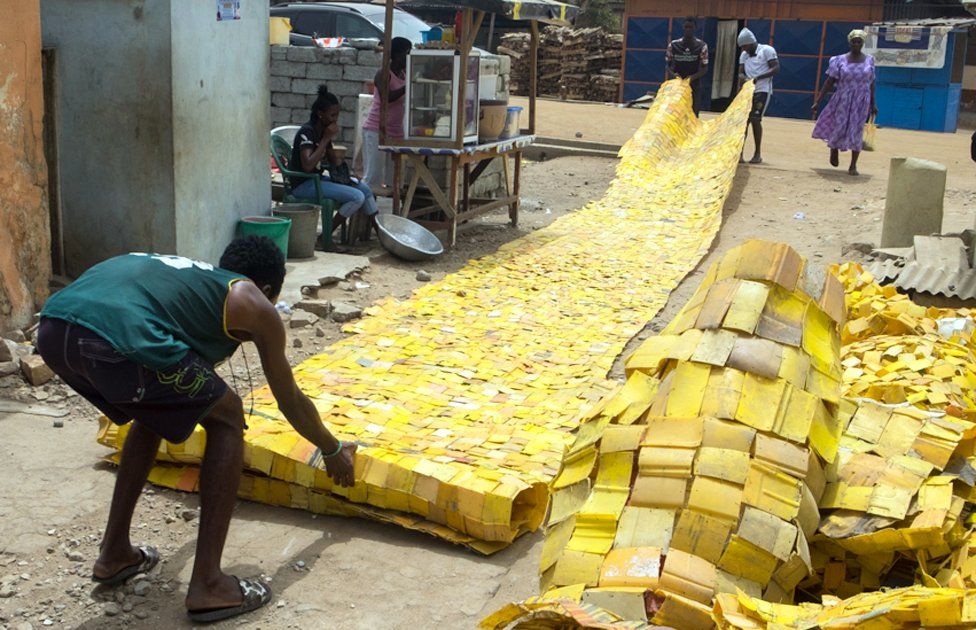 People rolling out yellow tapestry tapestry designed by artist Serge Attukwei Clottey on a road in La - Accra, Ghana