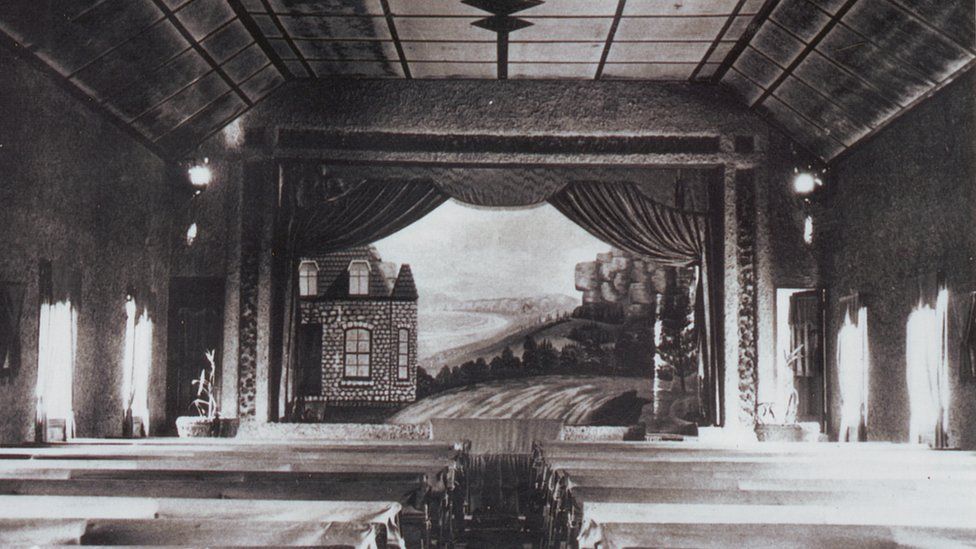 A black-and-white image from the 1940s showing the inside of a theatre, with a backdrop featuring a coastal scene