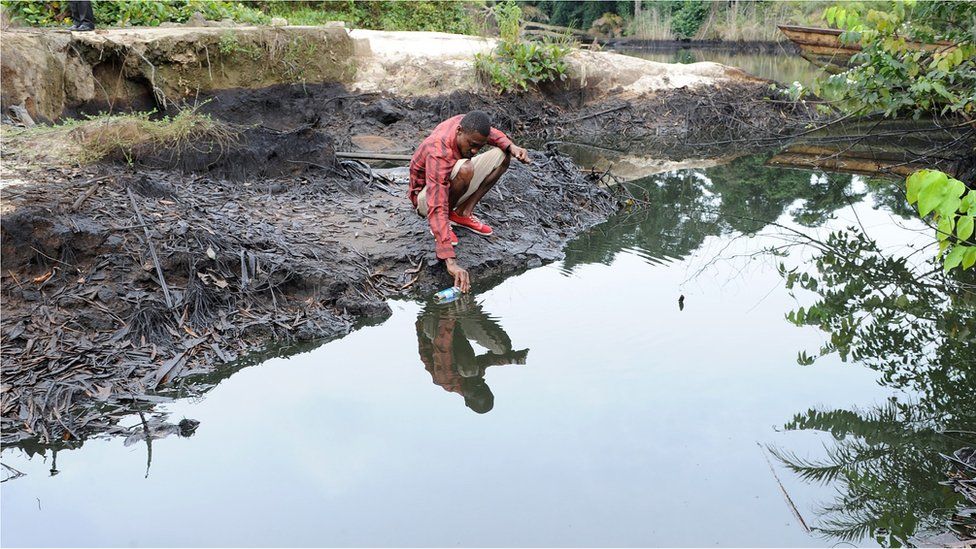 A man scoops spilled crude oil allegedly caused by Shell equipment failure floating at the bank of B-Dere waterways in Ogoniland, Rivers State, on August 11, 2011.