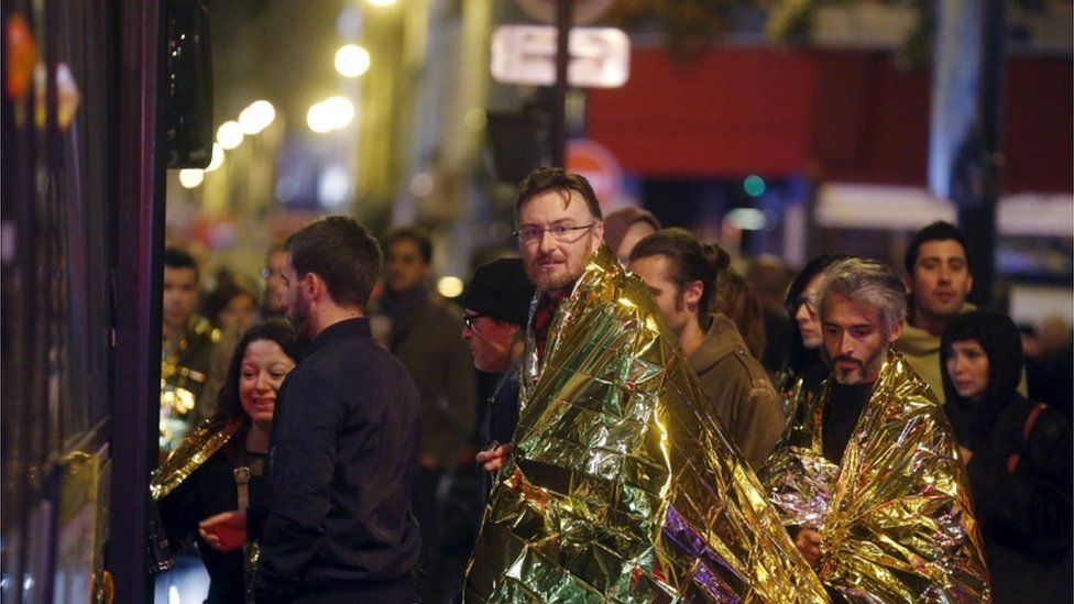 People warm up under protective thermal blankets as they prepare to board a bus to be evacuated near the Bataclan concert hall following fatal attacks in Paris, France, 14 November2015