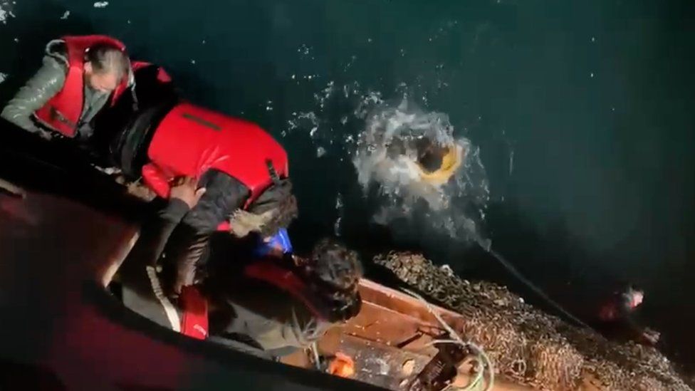 Migrants climbing into a trawler to escape the sea