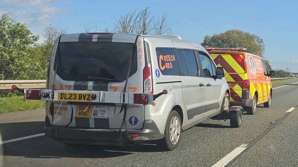 A silver taxi saying Creech Cabs on the window being towed by an RAC track