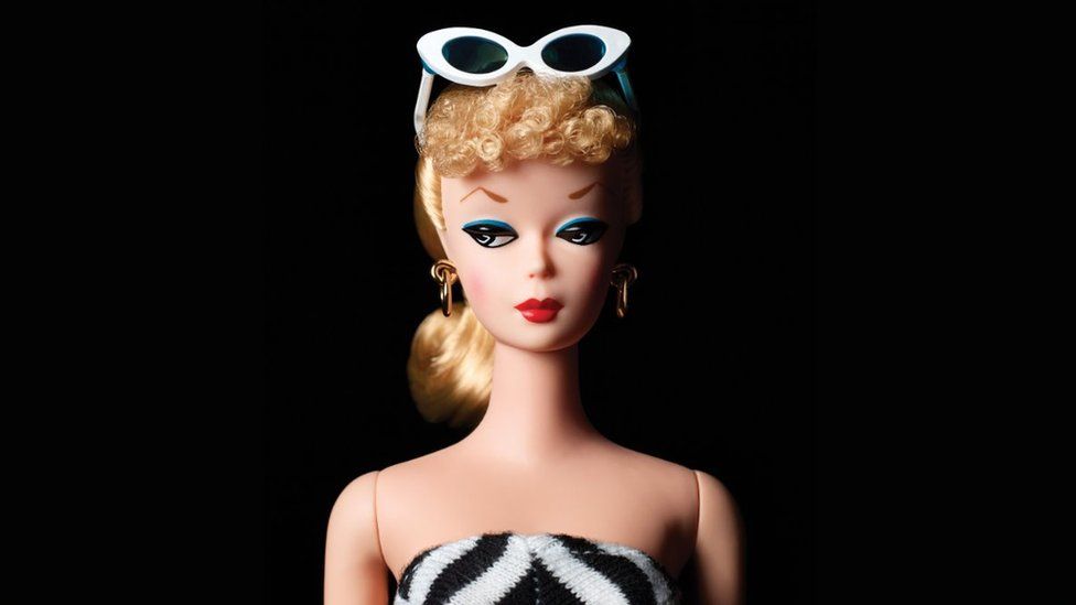 A traditional blonde Barbie doll in a black-and-white strapless bathing suit with white sunglasses on top of her head