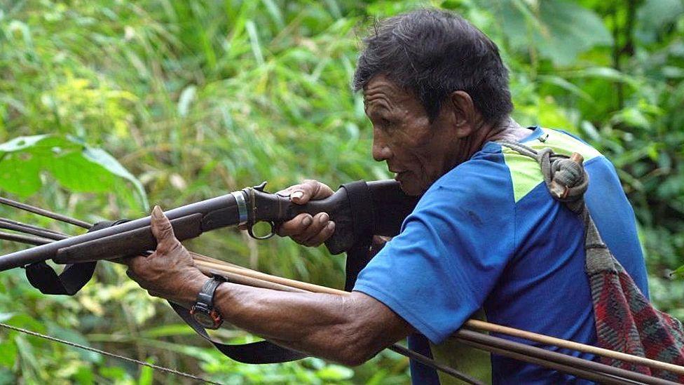 Juan in a blue T-shirt, aiming a gun 