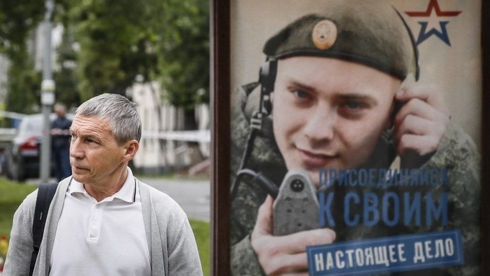 Man walks past conscription poster on bus stop in Moscow
