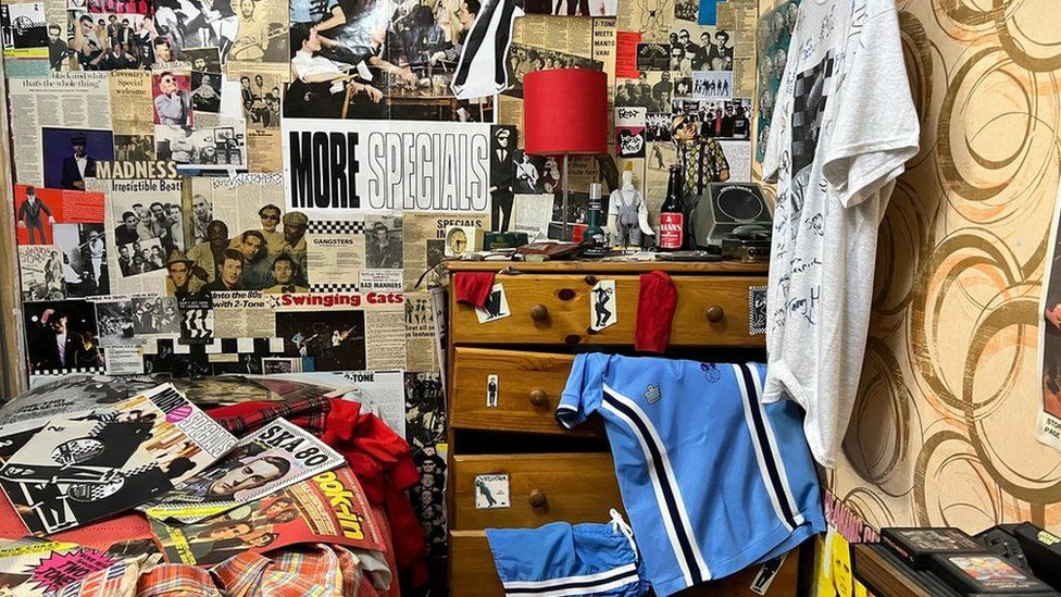 An exhibition showing a bedroom with a wall covered in posters