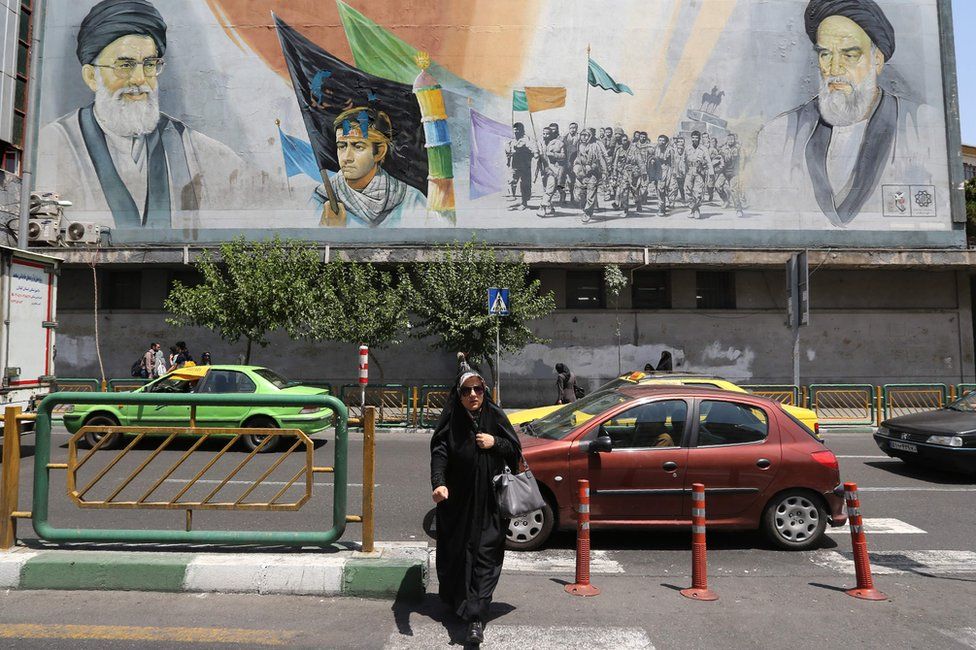 Iranian woman walks past a mural in Tehran showing Ayatollah Ali Khamenei (L) and Grand Ayatollah Ruhollah Khomeini (R) (25 June 2019)