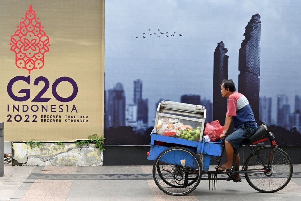 A fruit vendor rides his cart past a logo of the G20 Summit, in Jakarta on November 8, 2022.