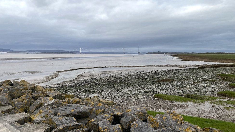 The Severn Estuary showing rocks in the foreground and the original Severn Bridge in the background