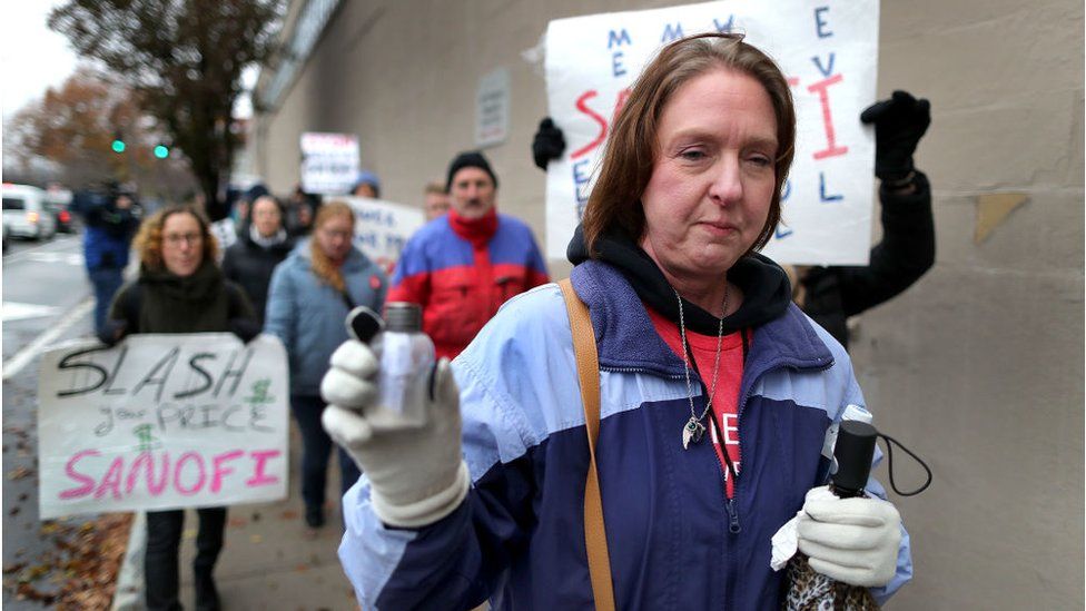 Alec Smith's mother holds a vial of her son's ashes during a protest against the high price of insulin outside Sanofi's offices in Massachusetts