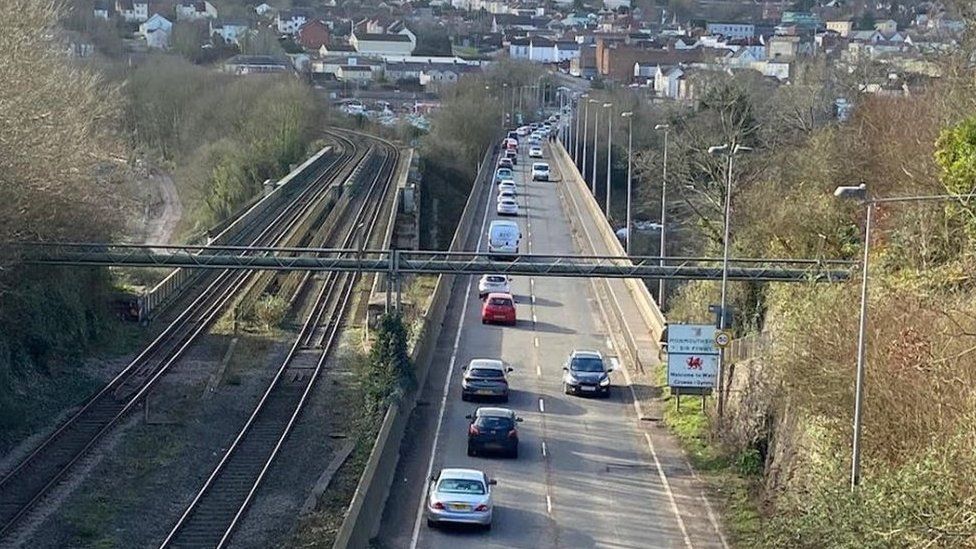 Traffic driving on the A48 next to a railway line with Chepstow in the distance