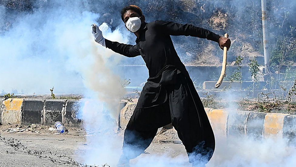 A Pakistan Tehreek-e-Insaf (PTI) party activist throws back a teargas shell toward police during a protest against the arrest of their leader, in Islamabad on May 10, 2023.
