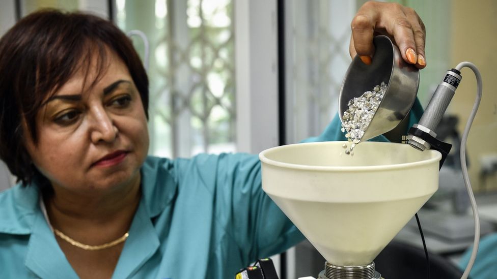 An employee pours rough diamonds into a funnel for weighing