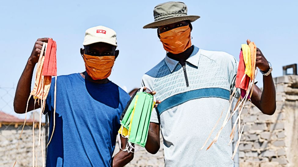 Men wearing and holding up face masks in South Africa's Nkowankowa Township during lockdown - 27 April 2020