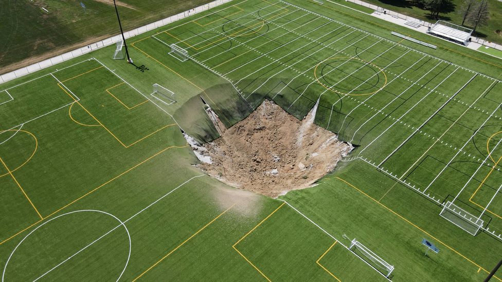A drone view shows a sinkhole, a large depression of brown soil with pieces of artificial turf hanging from the top edge into the hole, is seen in the middle of a multi purpose sports field at Gordon Moore Park in Alton, Illinois, USA, June 27 2024. 
