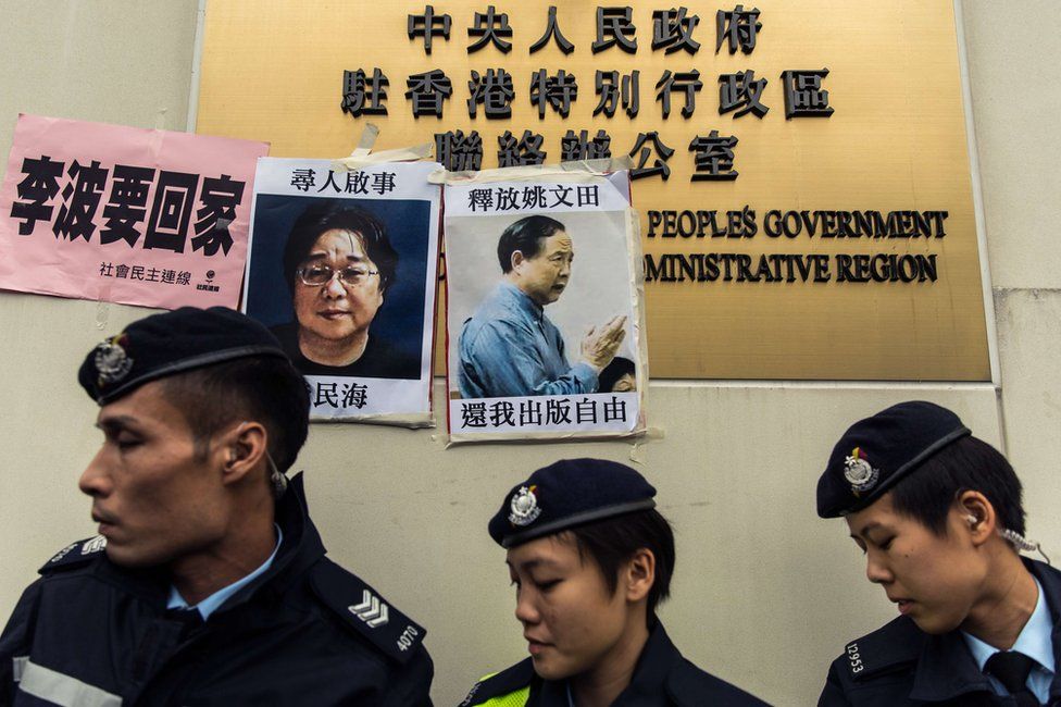 Police walk past missing person notices of Gui Minhai (L), one of five missing booksellers from the Mighty Current publishing house and Yau Wentian (R), a Hong Kong publisher who was last year jailed for 10 years while preparing to release a book critical of Chinese President Xi Jinping, posted on top of the sign of China"s Liaison Office in Hong Kong on 3 January 2016