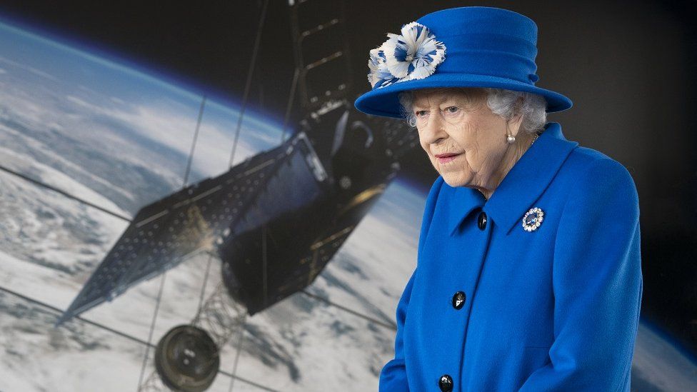 The Queen in front of a screen showing a satellite image