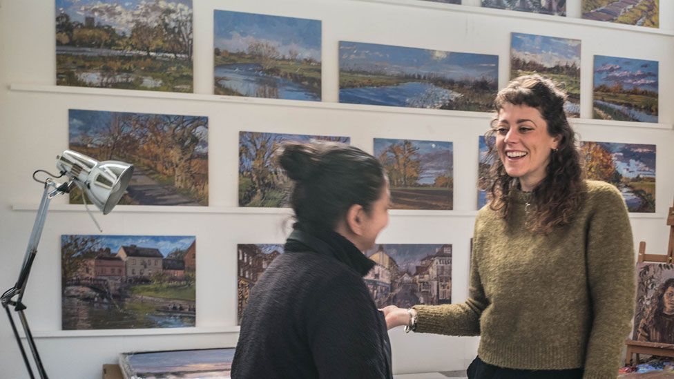 Sarah Allbrook during Cambridge Open Studioss with artwork behind and talking to a member of the public