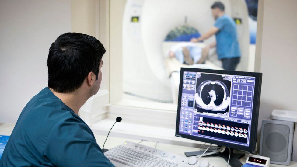 A generic picture of a doctor analysing a scan while a patient is in a scanner