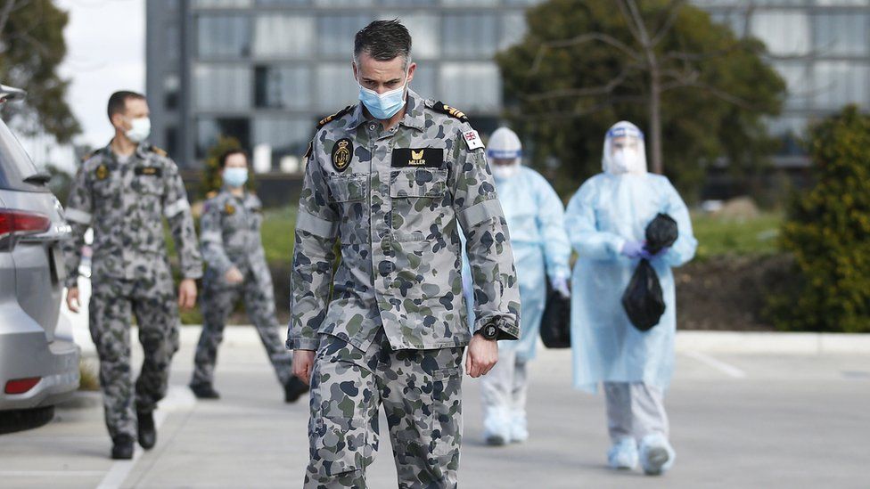 A soldier wearing a mask walks out of a nursing home with other medical responders