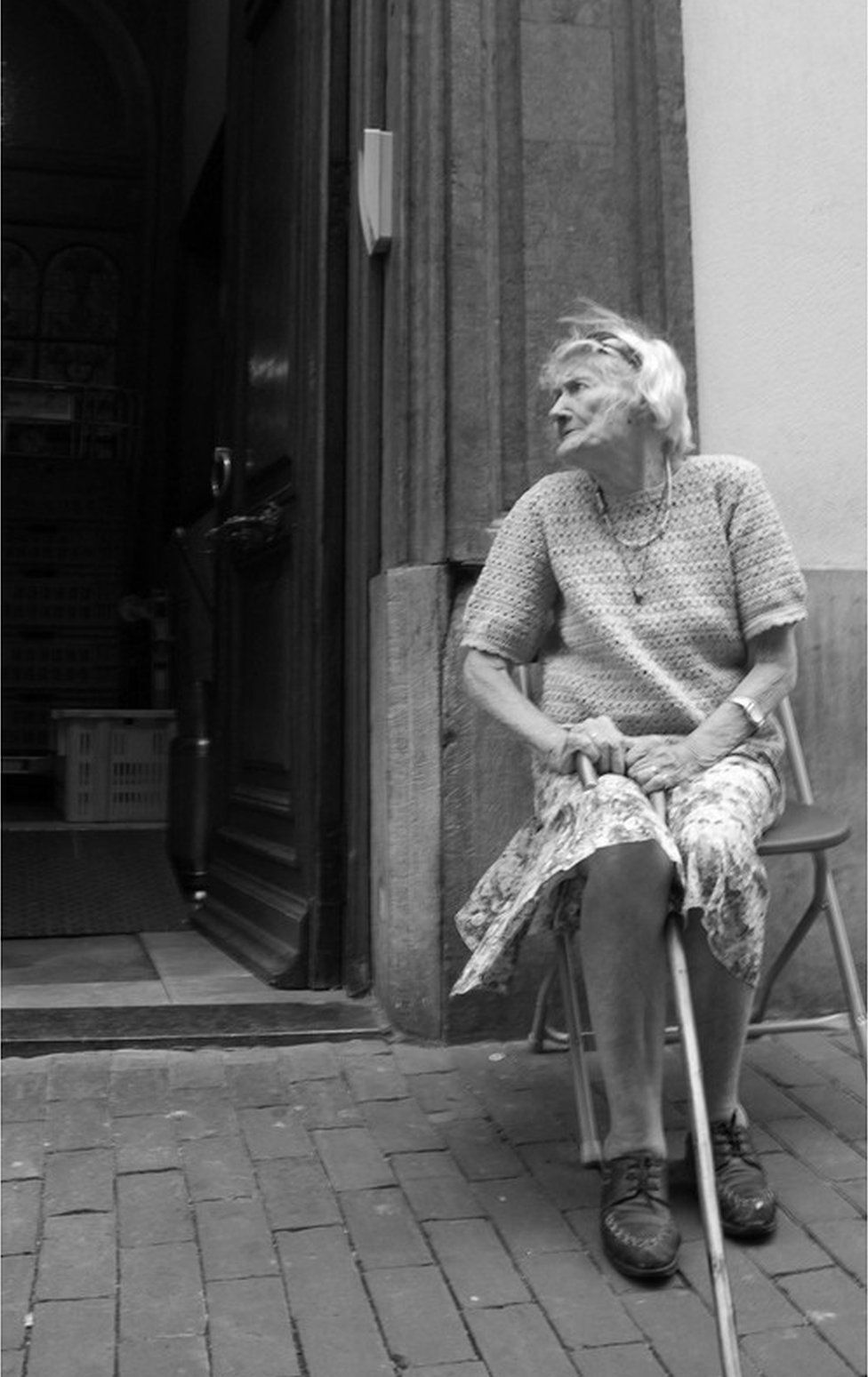 An elderly lady sits outside her doorway
