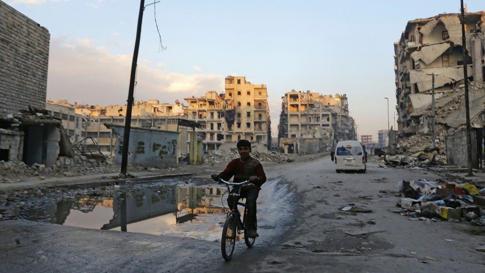 A Syrian boy rides his bicycle past destroyed buildings in Aleppo's formerly rebel-held al-Shaar neighbourhood on 21 January 2017, a month after government forces retook the northern Syrian city from rebel fighters