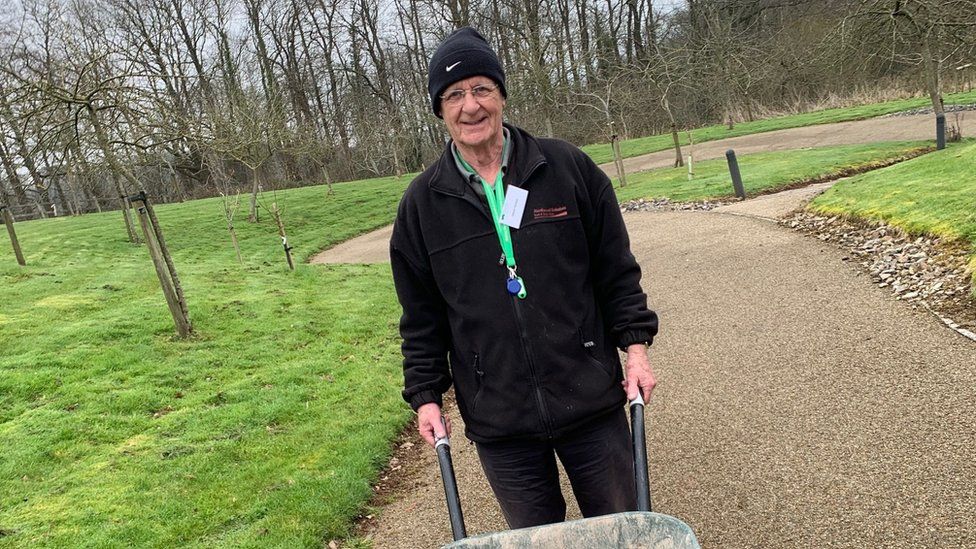 Dave Senior holding a wheelbarrow in a park area as he volunteers at Children's Hospice South West in Wraxall