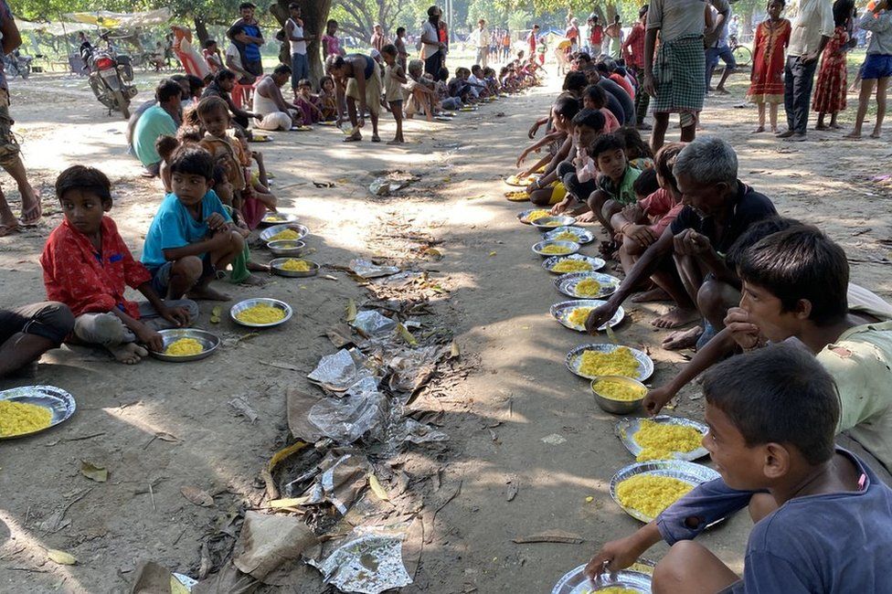 Children at the relief camp sit in the mud to eat their meals
