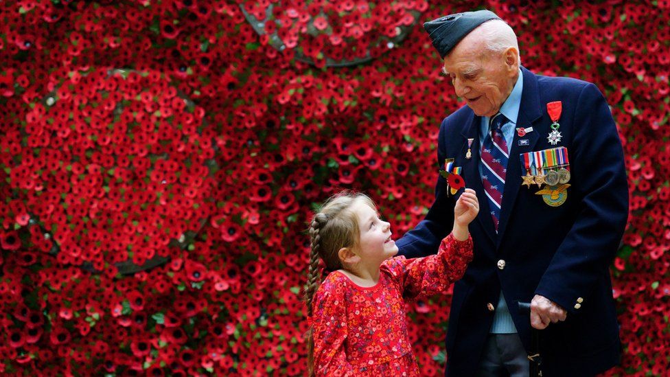 98-year-old D-Day Veteran Bernard Morgan, whose story is among those featured on the giant poppy wall, is given a poppy by Maya Renard, aged 6
