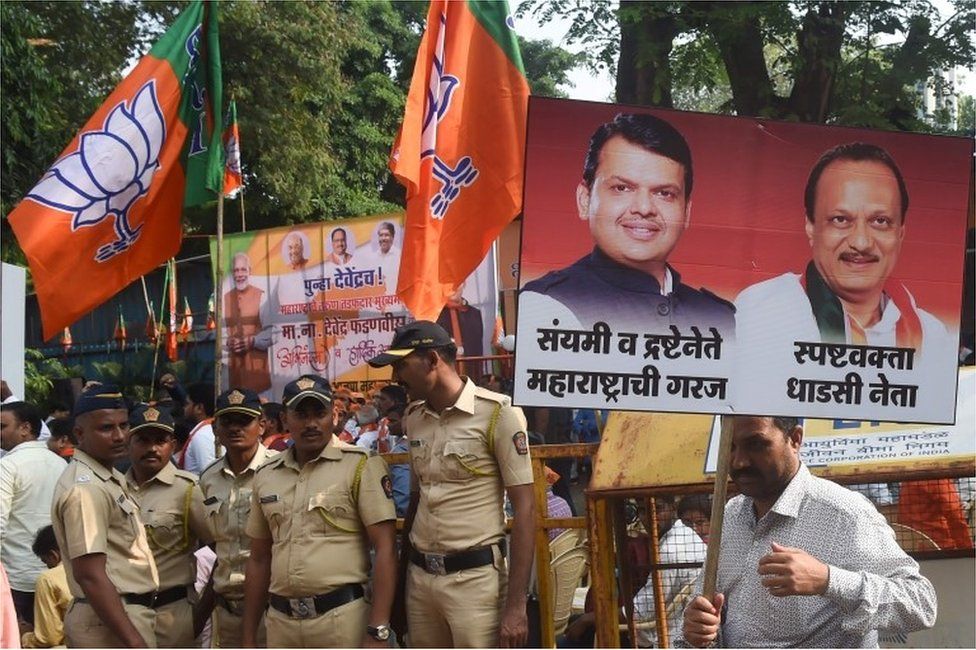 Bharatiya Janata Party (BJP) supporter carries a poster of Chief Minister of the western Indian state of Maharashtra Devendra Fadnavis and Nationalist Congress Party (NCP) leader and deputy Chief Minister Ajit Pawar at a victory rally outside the headquarters in Mumbai on November 23, 2019.